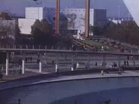 An elevated shot looking down at an arched reflecting pool and visitors walking on surrounding paths.