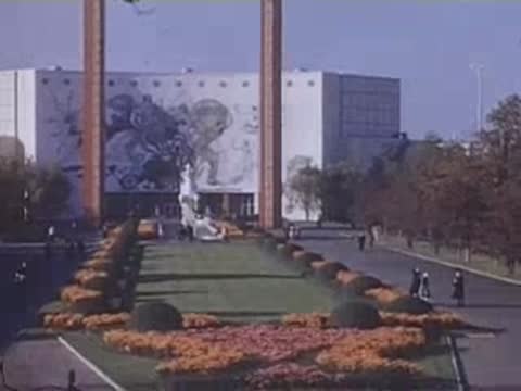 A decorative garden bed filled with colorful flowers in front of a large white pavilion with a painted mural.