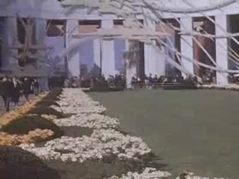 Pan right across manicured lawns towards modernistic white pavilions at the New York World's Fair.
