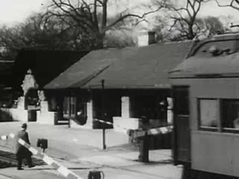 Train passing a station with crossing gate lowering, 1940s