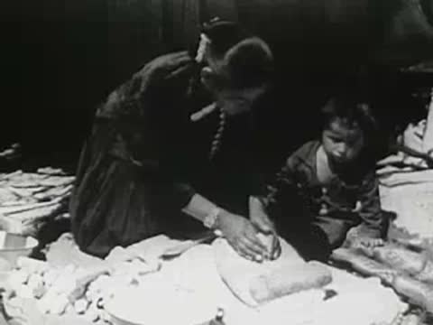 Person molding clay or adobe with a child helping outdoors