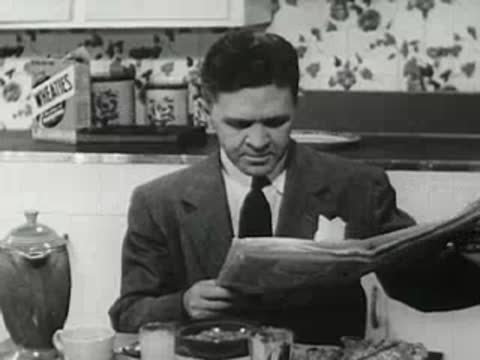 Man reading a newspaper at the breakfast table with Wheaties box