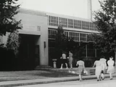 People walking toward the entrance of a factory building, vintage educational film.