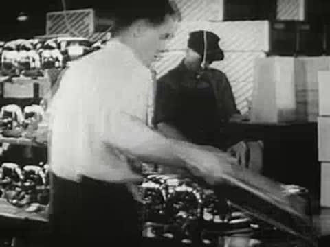 Factory worker moving a tray of assembled toasters, vintage industrial film.