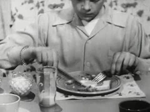 Close-up of a young boy eating breakfast and using a toaster at a table.