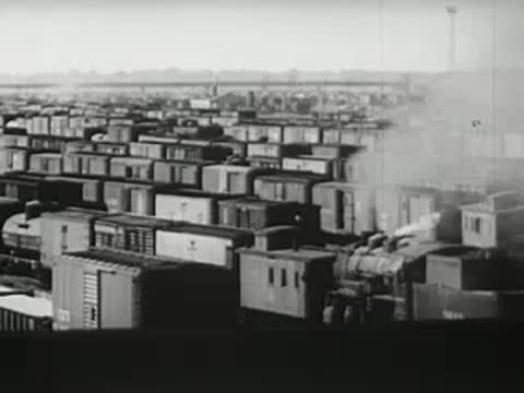 Aerial or high-angle view of a freight yard with many train cars and steam, 1940s.