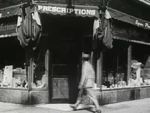 Person walking past the window of a 1940s pharmacy storefront