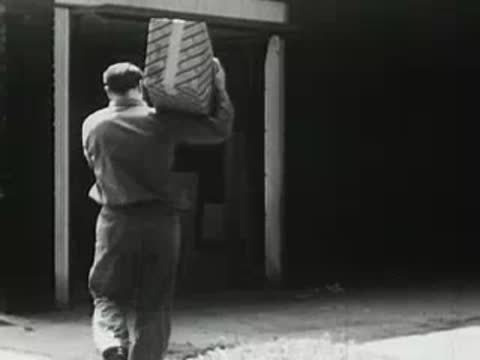 Worker carrying a boxed product out of a warehouse or freight car, historical film.