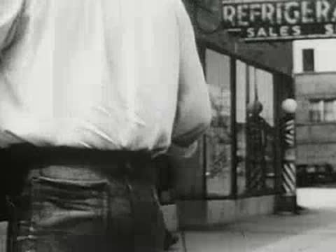 Man walking past a storefront window on a city street, 1940s educational film.