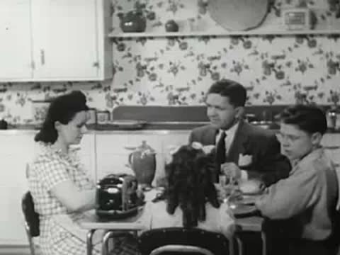 Family sitting at a kitchen table having breakfast with a toaster nearby, vintage film.