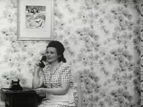 Woman talking on a telephone in a room with patterned wallpaper, 1940s film.