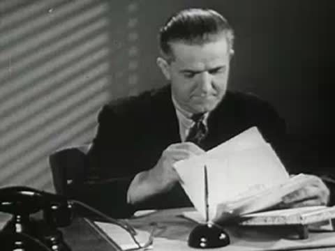Man sitting at a desk reviewing documents and talking on a telephone, vintage office scene.