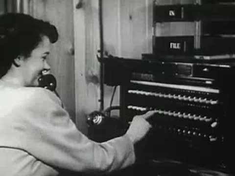 Operator using telephone switchboard in 1940s office.