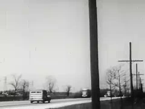 Telephone pole along suburban street with passing vehicles, 1940s.