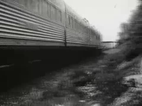 Passenger train speeding along tracks near wooded embankment, 1940s.