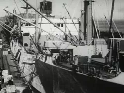 Cargo ship docked at harbor with cranes, 1940s.