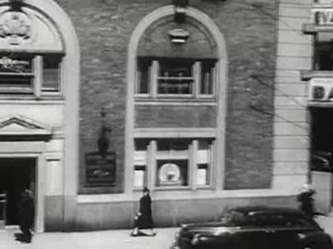 Downtown street view with storefronts and cars, 1940s.