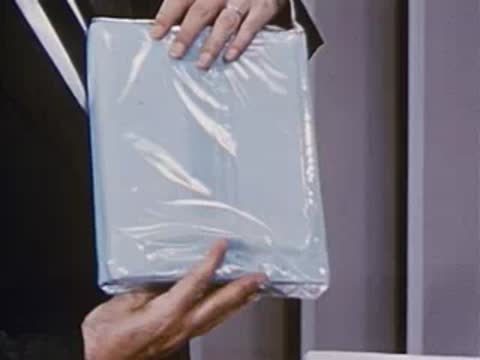 Man in suit holds up wrapped shirt package against gray background