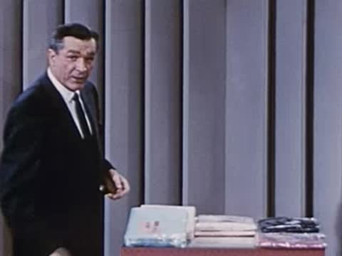 Man in suit places shirt packages on a desk in studio