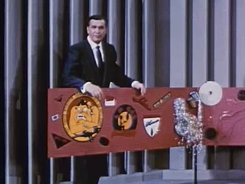Man in suit opens hinged display board with various materials attached