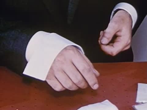 Close-up of hands folding a white strip of material at desk