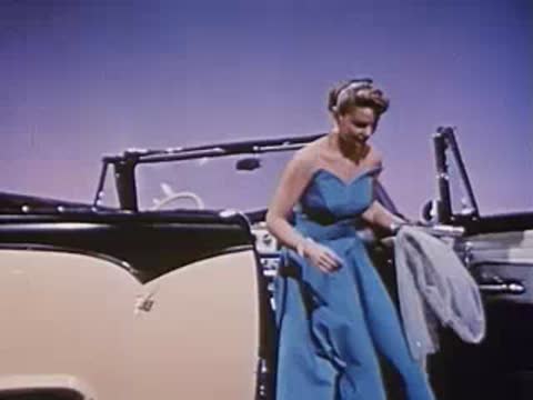 Woman stands next to convertible car holding a garment bag