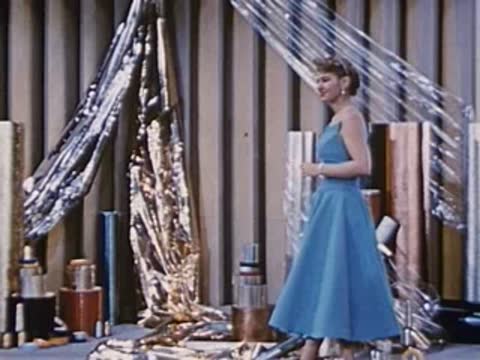 a woman in a blue gown walks past shiny materials in a factory