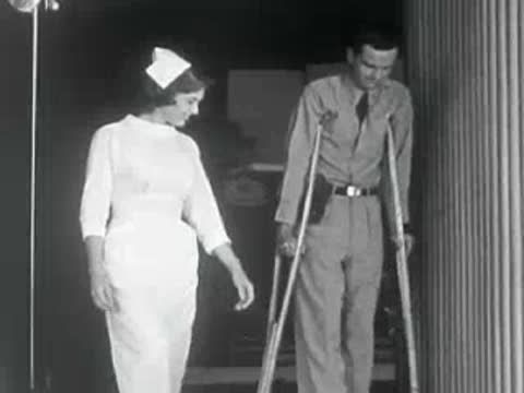 A nurse and an injured soldier on crutches stand outside a building.