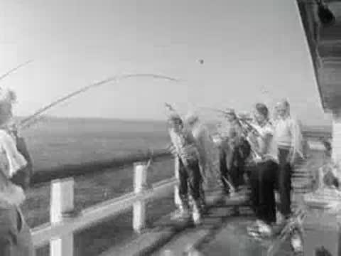 Fishermen and onlookers on a wooden pier reacting excitedly as fish are caught.
