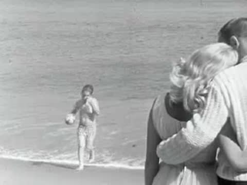 A couple embraces on the beach while a child plays nearby.