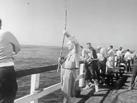 People on a pier reeling in fish with rods while looking out at the ocean.