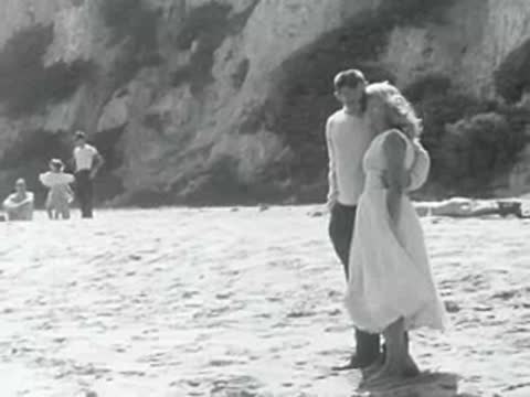 A couple stands on the beach as a child approaches.