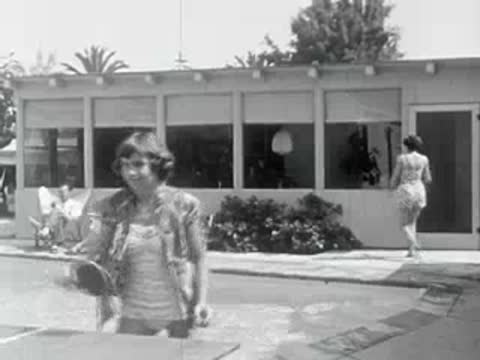 A woman plays table tennis by a swimming pool.