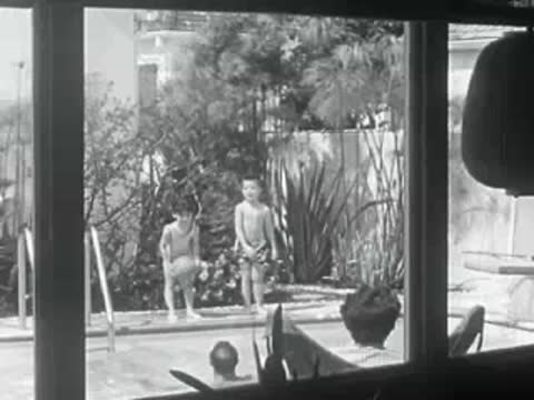 Two children stand by a backyard swimming pool in 1950s California.