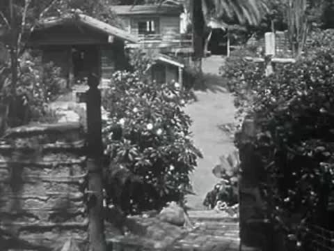 A person walks past a stone-paved garden gate in 1950s California.