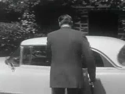 A man in a suit gets into a classic car in 1950s California.