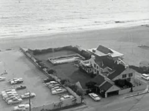 Aerial view of a coastal house and parked cars in 1950s California.
