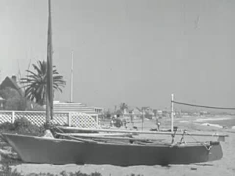 A sailboat rests on a sandy beach in 1950s California.