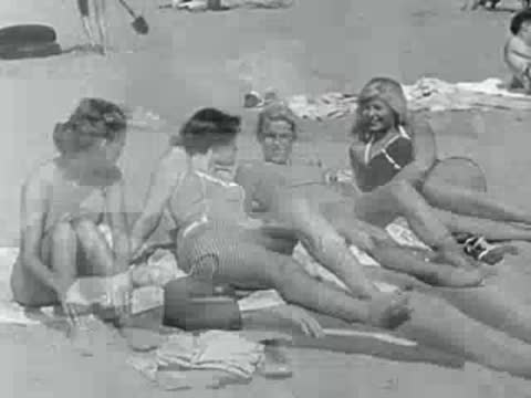 Four women in swimsuits relax on a sandy beach in 1950s California.