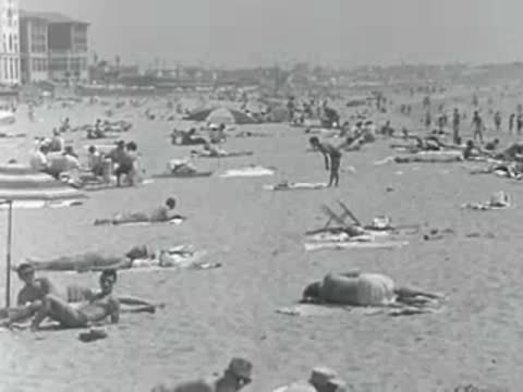 People relax on a crowded beach with umbrellas in 1950s California.