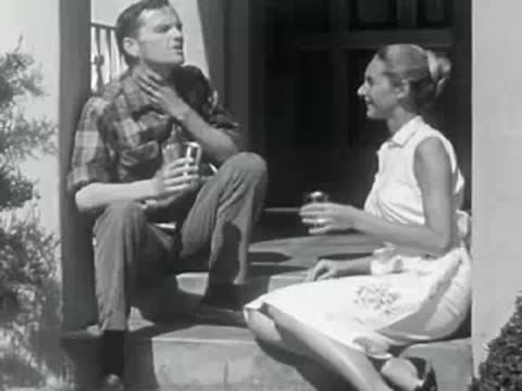 A man and woman sit and converse on the steps of a house.