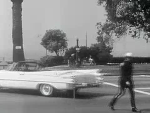 A police officer walks across the street next to a parked convertible.