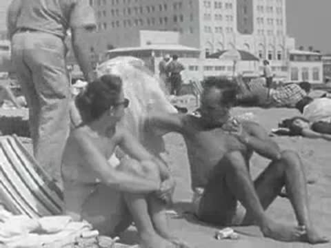 People relax in beach chairs on the sand with buildings behind them.