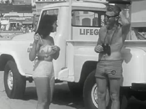 A lifeguard truck is parked on the beach with a man and woman nearby.