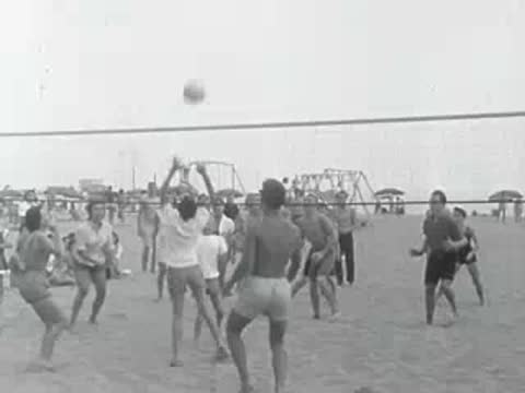 A large group of people play beach volleyball on a net court.