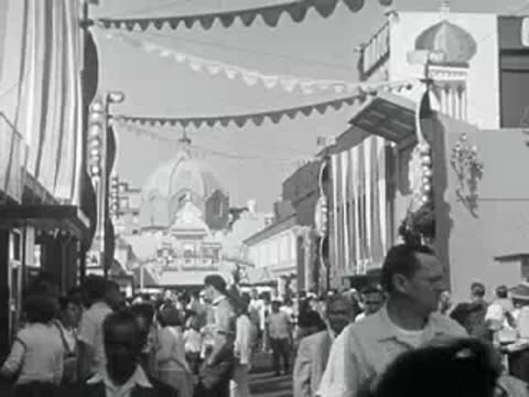 A bustling crowd of visitors walking along a decorated amusement park street.