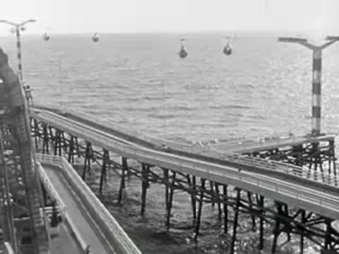 View of a pier extending into the sea with cable cars in the distance.