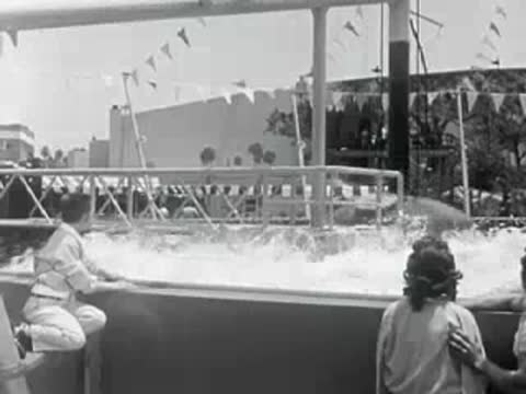 Amusement park boat ride splashing into the water with spectators watching.