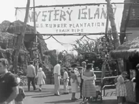 Visitors walking past a 'Mystery Island' train ride entrance sign at the park.