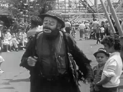 A clown interacting with children near a crowd at the amusement park.